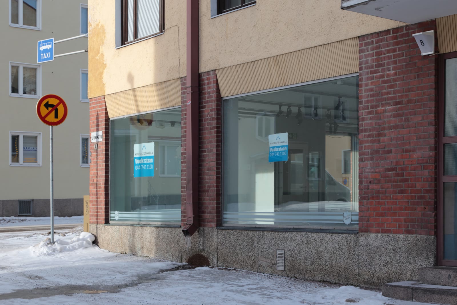 An empty corner retail unit with bare display windows and letting notices taped to the glass.